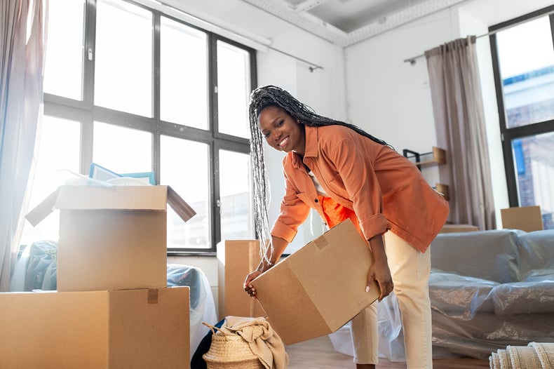 A Black woman unpacking a moving box in a room